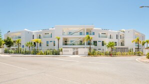 A modern multi-story building with a central staircase, surrounded by a parking lot and palm trees. - Apartment  by Interhome (Albufeira)