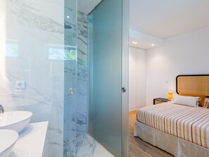 Une chambre d’hôtel moderne dotée d’une salle de bain avec un lavabo en marbre et une douche à parois de verre.