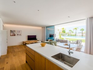 Une cuisine moderne dotée d’un grand îlot central, d’un coin repas avec une table ronde et d’une vue sur une piscine et la verdure environnante.