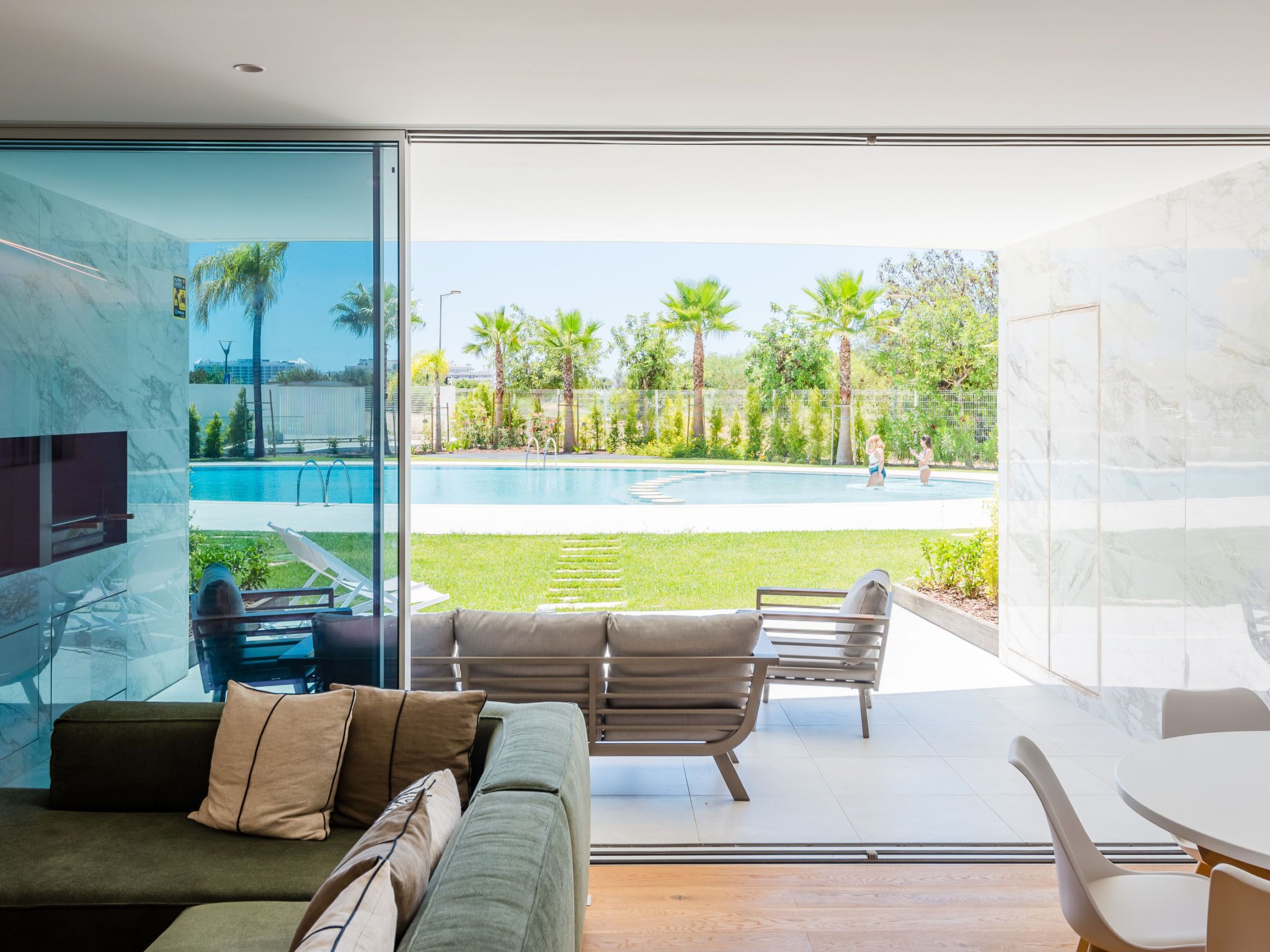 A modern living room with a glass wall, a pool, and outdoor seating.