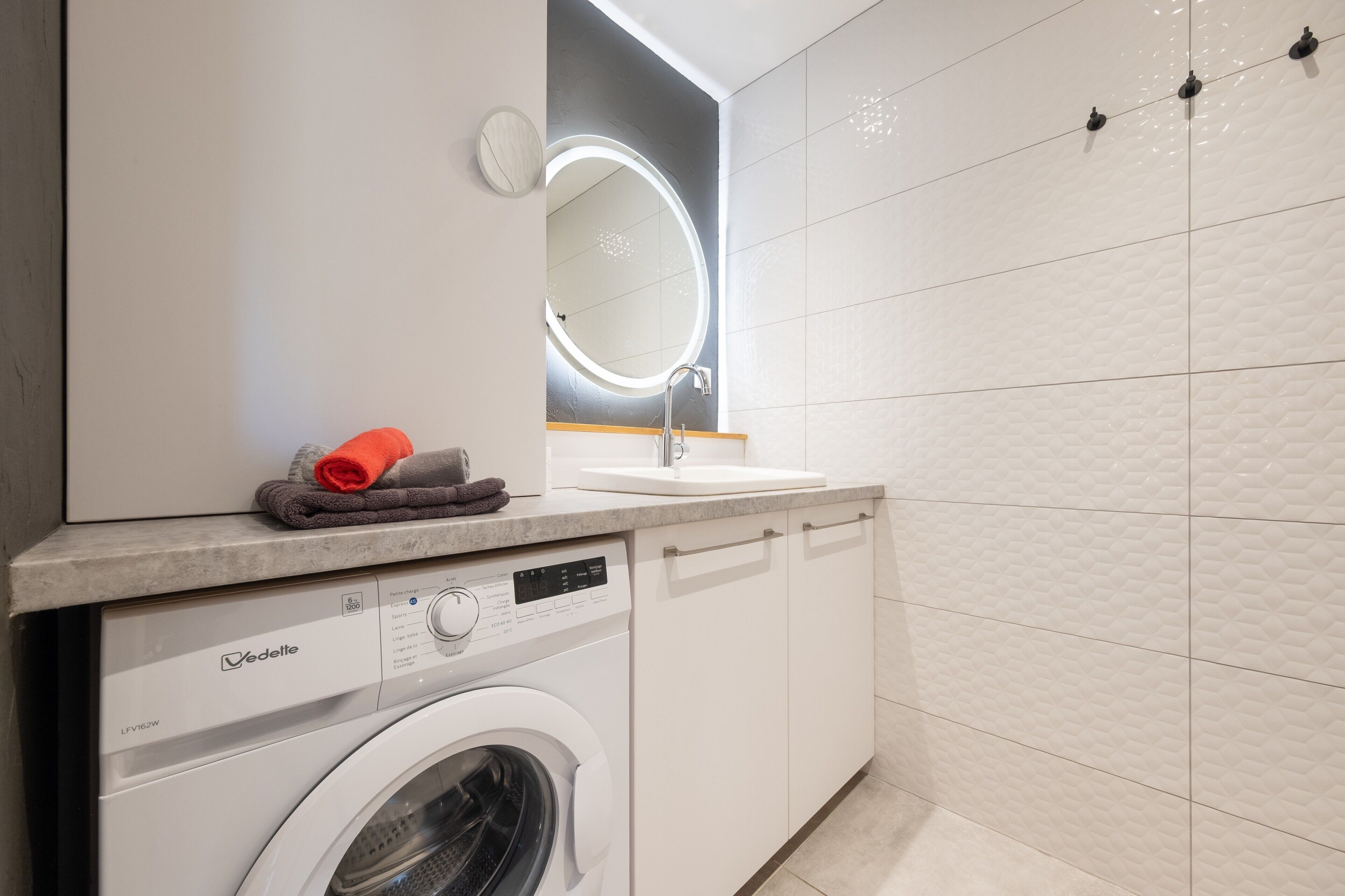 A modern bathroom with a washing machine, a sink, and a mirror with a light.