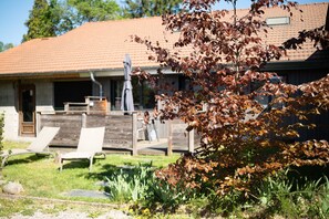 A building with a tiled roof, a covered patio area with two lounge chairs, and a garden with a tree.