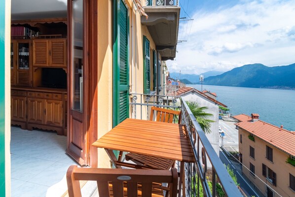 Ein Balkon mit Holztisch und Stühlen, mit Blick auf ein Gewässer und Gebäude.