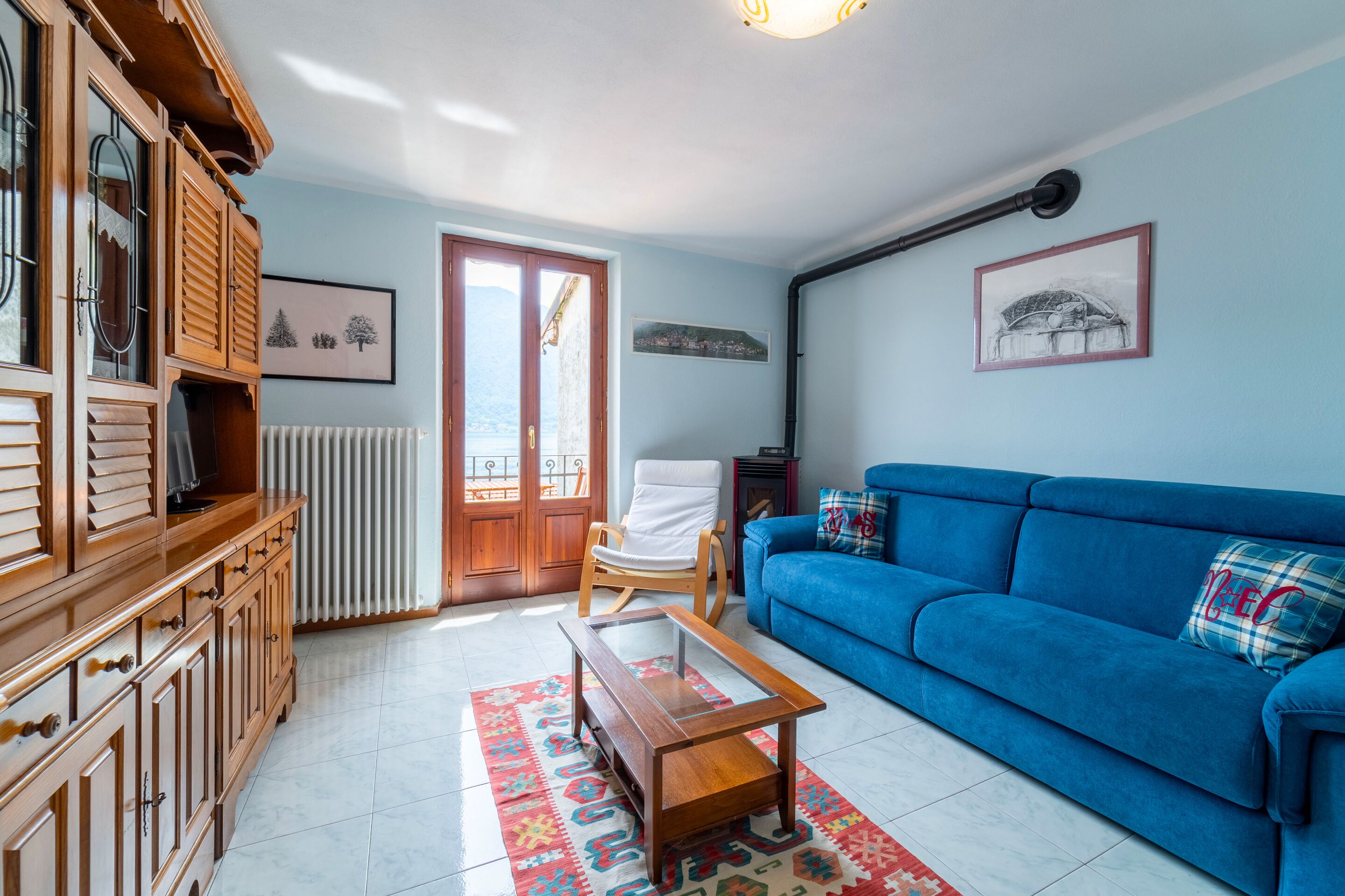 Una sala de estar con un sofá azul, un mueble de madera y una mesa de centro de cristal.