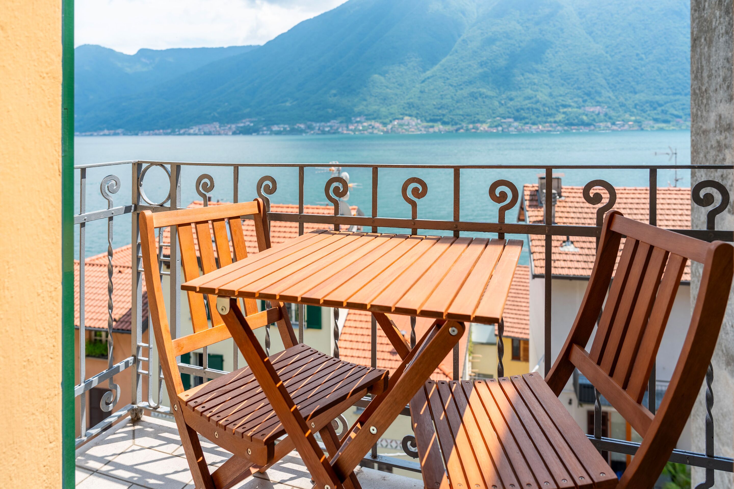 A balcony with a table and chairs, overlooking a lake and mountains.