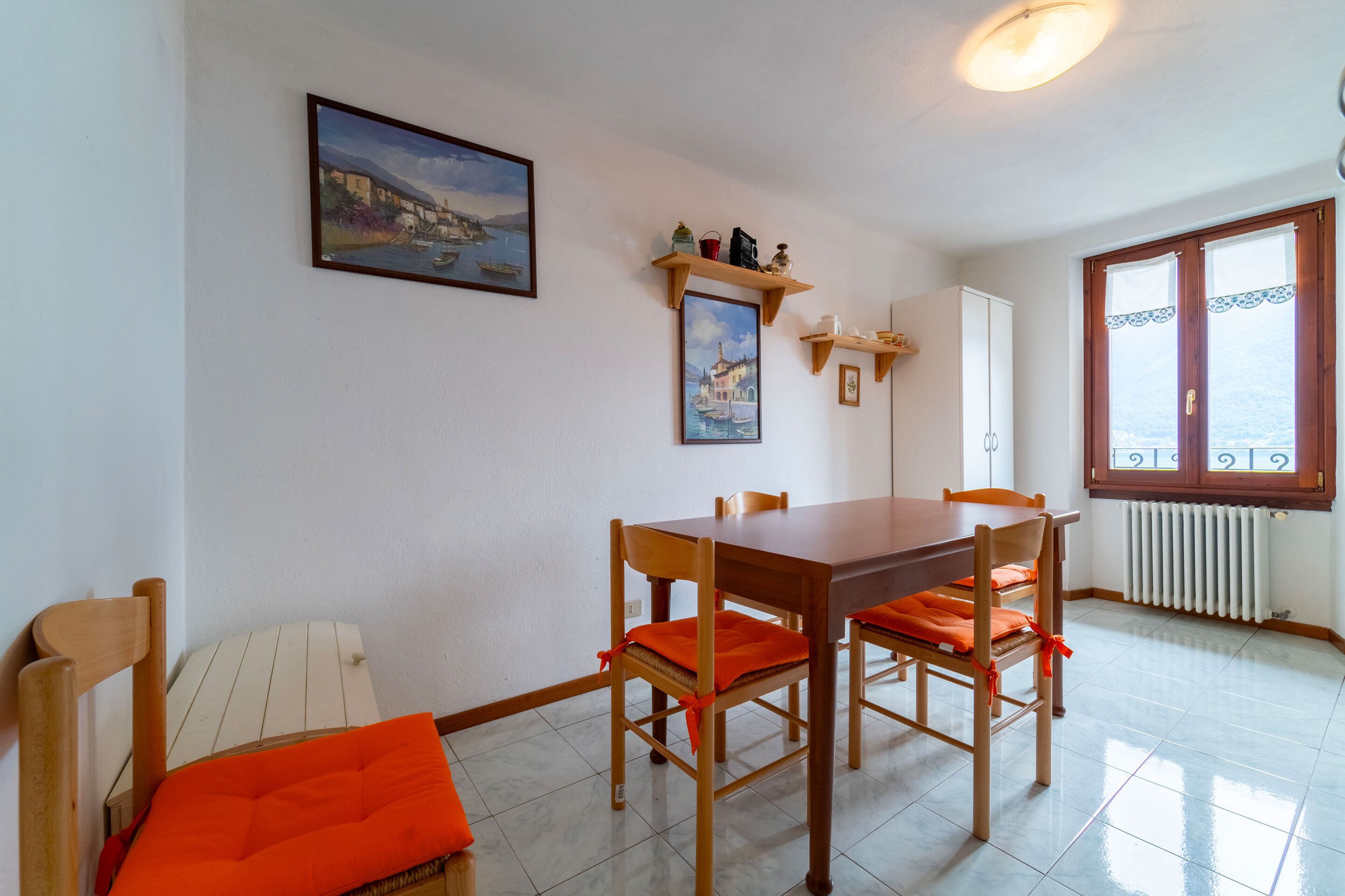 Un coin repas avec une table et des chaises en bois, un radiateur blanc et une fenêtre donnant sur un paysage agréable.