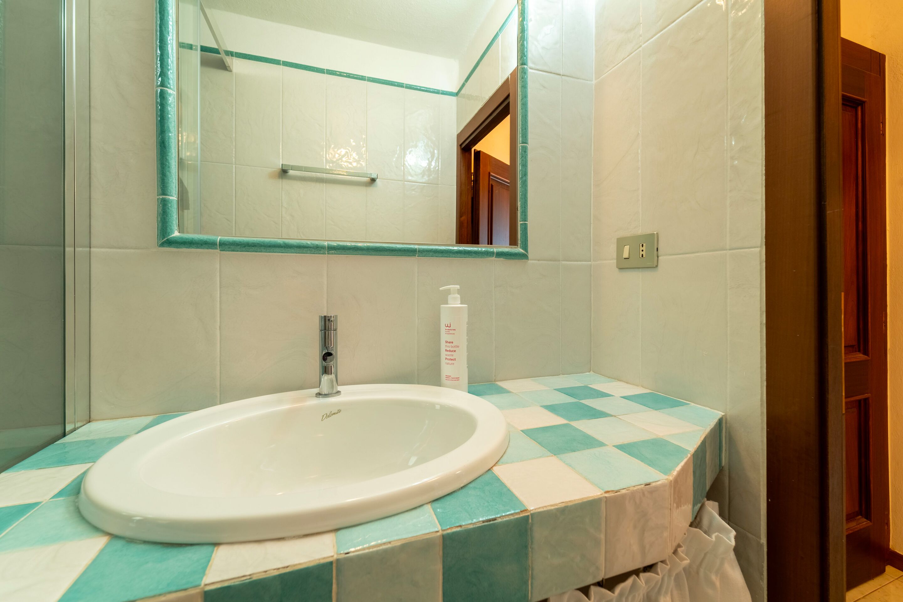 A bathroom with a white sink, a mirror with a teal frame, and checkered tiles.