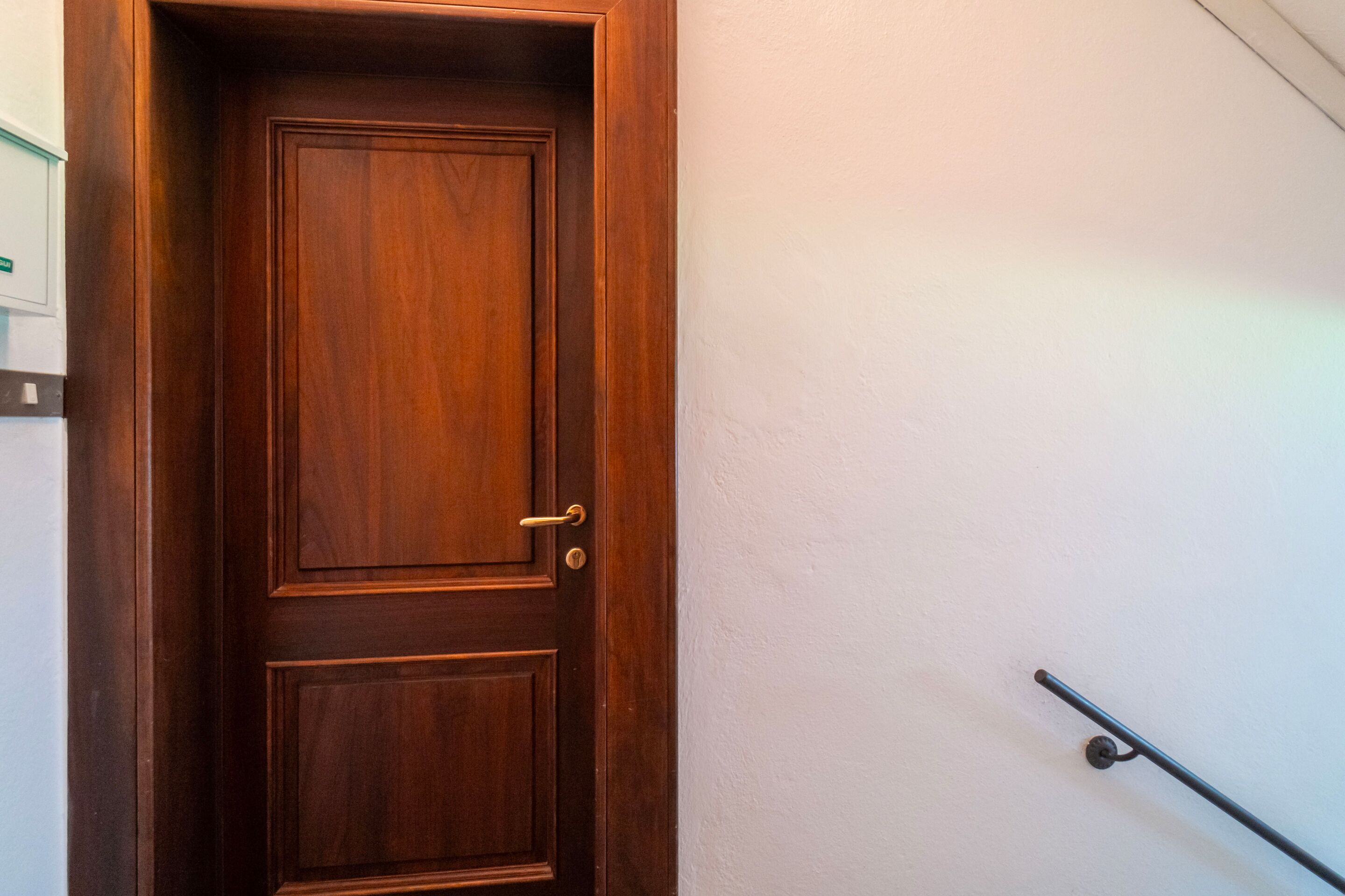 Una puerta de madera con manija y un pasamanos de metal en la pared contigua.