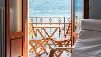 Ein Holztisch und -stühle auf einem Balkon mit Blick auf einen See und Berge.