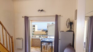 Ein Zimmer mit Bett, Esstisch mit Stühlen, Heizkörper, Deckenventilator und Blick auf Gebäude.