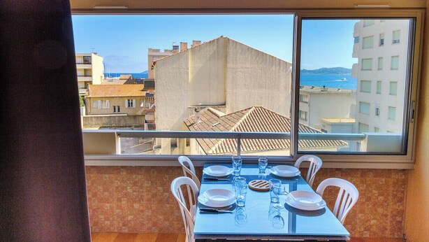 Ein Balkon mit Tisch für zwei Personen, Blick auf eine Stadtlandschaft mit Gebäuden und Meer.