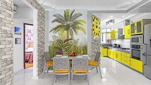A modern kitchen with yellow cabinets, a large clock, and a dining area with a table and chairs. - Jaddoo Apartment at Azeer Residence (Grand-Baie)
