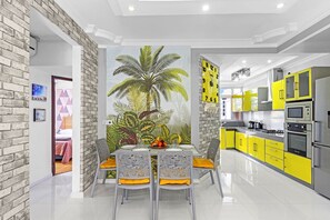 A modern kitchen with yellow cabinets, a large clock, and a dining area with a table and chairs. - Jaddoo Apartment at Azeer Residence (Grand-Baie)