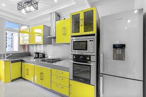 A modern kitchen with yellow cabinets, stainless steel appliances, and a built-in oven. - Jaddoo Apartment at Azeer Residence (Grand-Baie)
