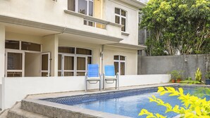 A swimming pool with steps leading up to it, two blue chairs, and a building with multiple windows. - Jaddoo Apartment at Azeer Residence (Grand-Baie)