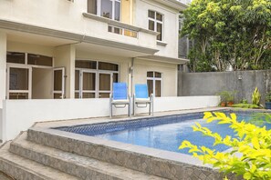 A swimming pool with steps leading up to it, two blue chairs, and a building with multiple windows. - Jaddoo Apartment at Azeer Residence (Grand-Baie)