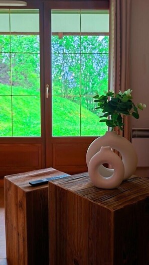 A wooden table with a vase and a remote control, a wooden door with a view of green trees, and a window with a curtain. - Skiing, terrace, swimming pool: ideal apartment (Flumet)