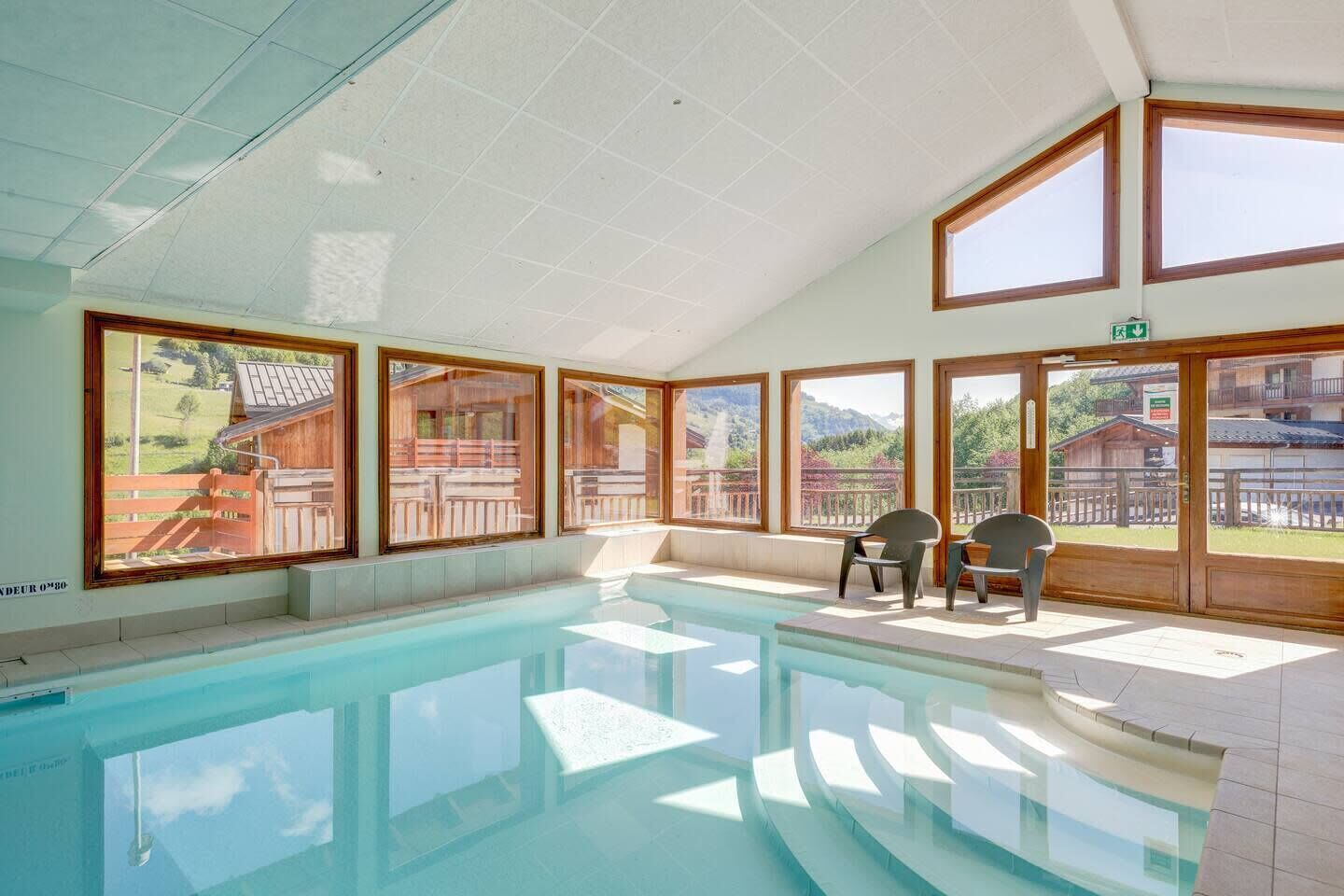A swimming pool with clear views of the outdoors, including a wooden deck and a mountain backdrop.