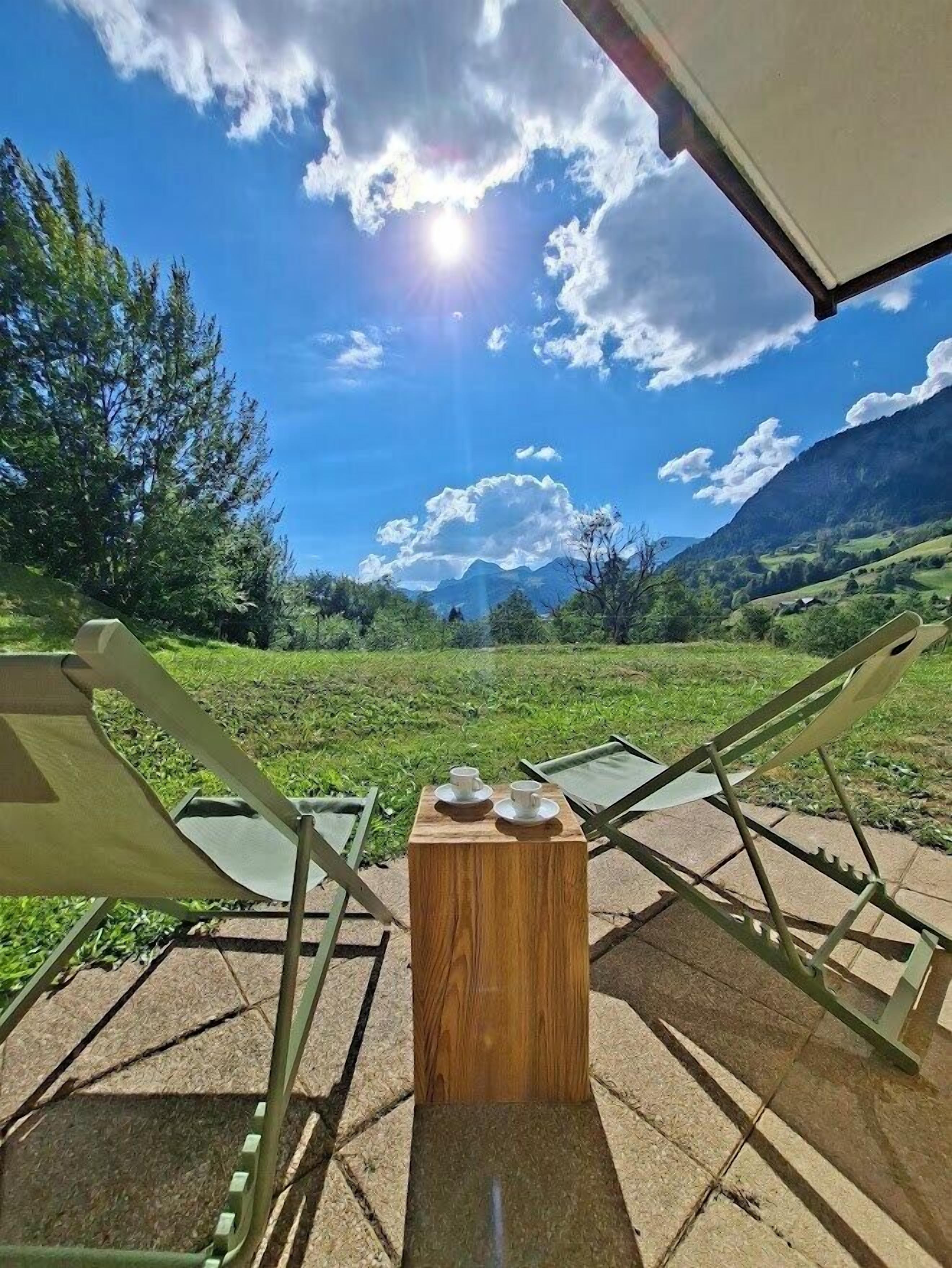 A campsite with a wooden table and chairs facing a mountainous landscape.
