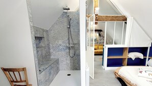 Een badkamer met een douche, een houten stoel en een bed met een blauw hoofdeinde.