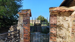 Een bakstenen poort met een metalen hek, leidend naar een stenen muur en een heldere lucht.