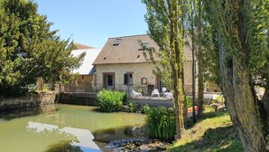 Uitzicht op een rivier met een stenen gebouw, een vijver met waterlelies en een boom.