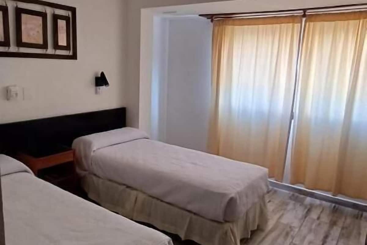 A room with two beds, a ceiling fan, a wall-mounted phone, and a window with curtains.
