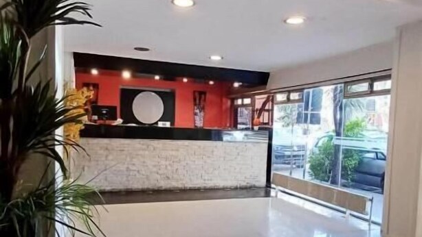 A spacious lobby with a reception desk, a large potted plant, and a view of the street through large windows. - Cadi Palace (Mar del Plata)