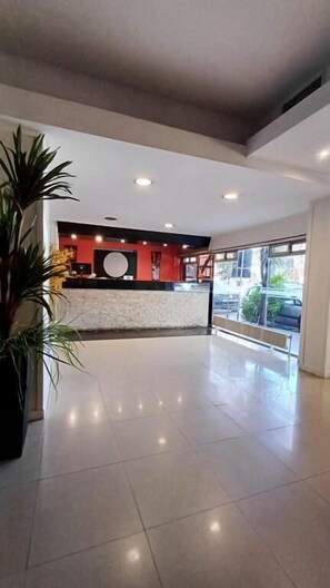 A spacious lobby with a reception desk, a large potted plant, and a view of the street through large windows. - Cadi Palace (Mar del Plata)
