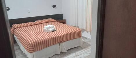 A bedroom with a bed, a nightstand, a wall-mounted light, and a curtain.