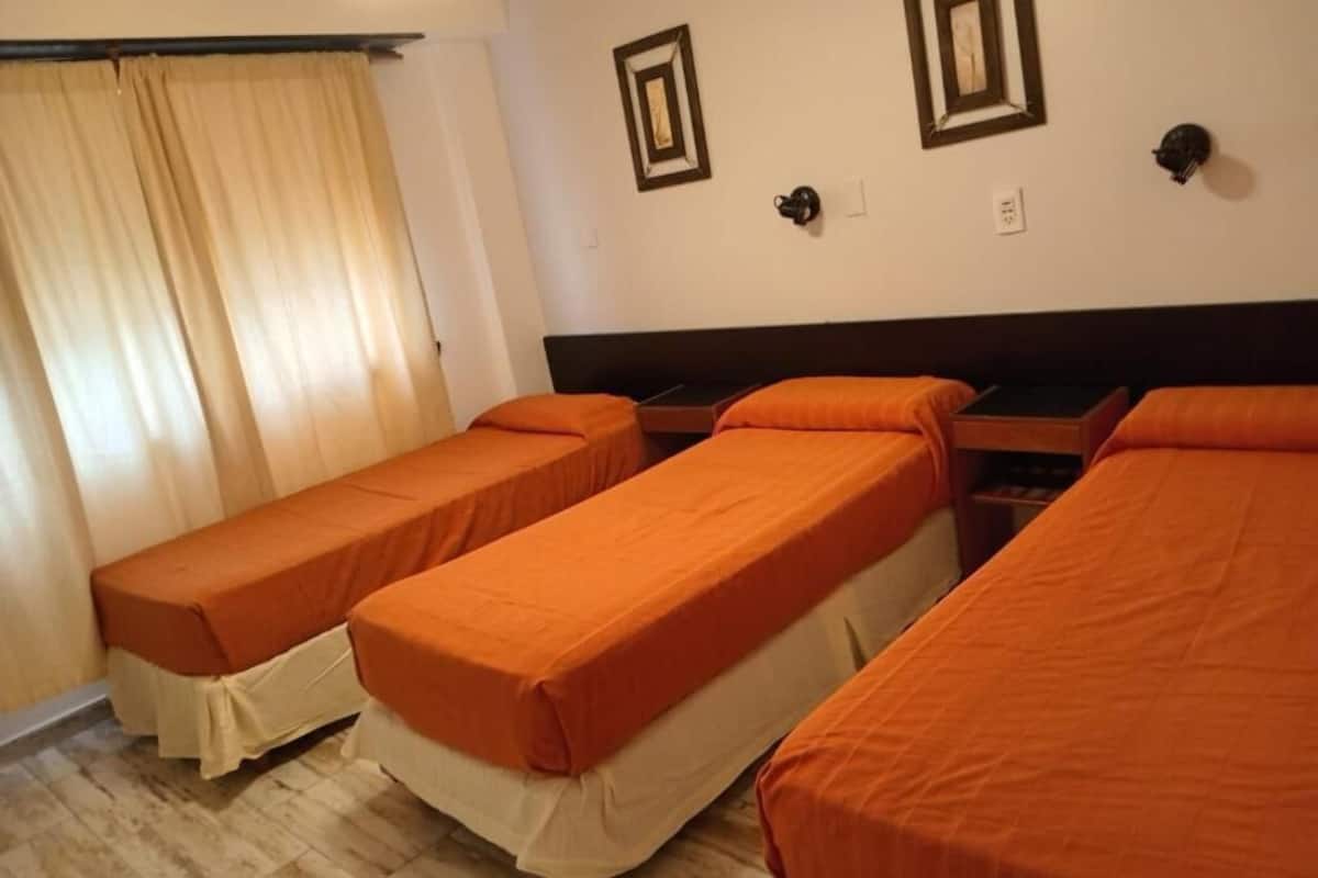 A room with three single beds, a curtain, a wall-mounted lamp, and a framed picture.