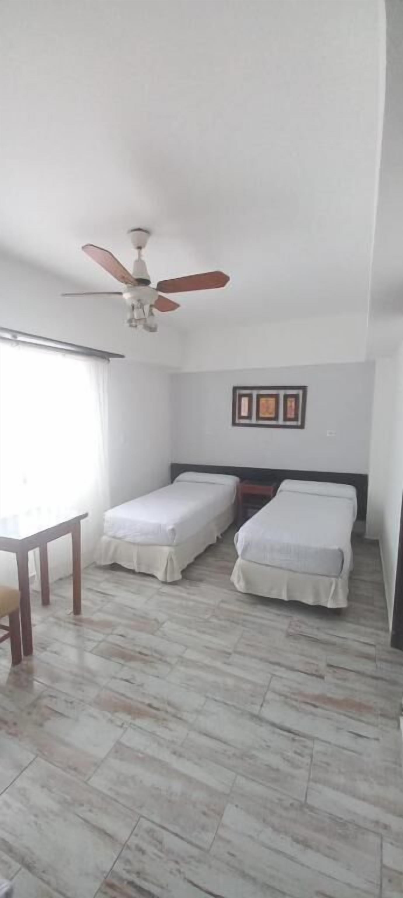 A room with two beds, a ceiling fan, a table, and a window.