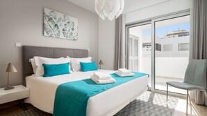 Ein modernes Hotelzimmer mit einem großen Bett, Blick durch eine Schiebetür und einem grauen Sessel.
