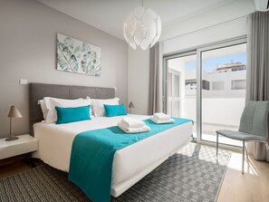 Ein modernes Hotelzimmer mit einem großen Bett, Blick durch eine Schiebetür und einem grauen Sessel.