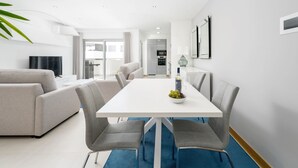 Ein modernes Wohnzimmer mit einem weißen Esstisch, grauen Sofas und einem blauen Teppich.