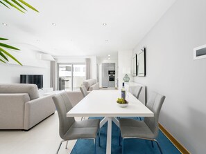 Ein modernes Wohnzimmer mit einem weißen Esstisch, grauen Sofas und einem blauen Teppich.