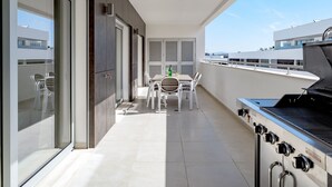 Ein moderner Balkon mit Grill, einem Esstisch und Stühlen sowie Blick auf die Stadtlandschaft.