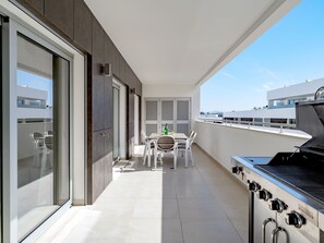 Ein moderner Balkon mit Grill, einem Esstisch und Stühlen sowie Blick auf die Stadtlandschaft.