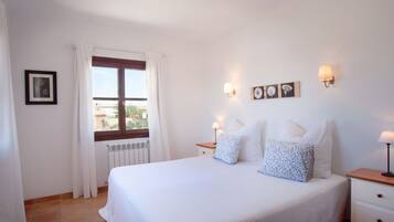 Hotellihuone, jossa on suuri sänky, kaksi yöpöytää, ikkuna verhoilla ja seinään kiinnitetyt lamput.