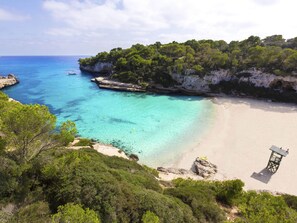 A beach with clear turquoise water, a sandy shore, and a rocky cliff with vegetation. - Sa Bassa by Interhome (Cala Llombards)