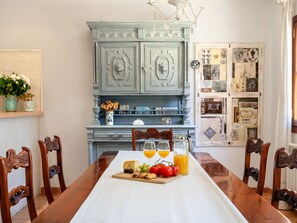 A dining table with a white tablecloth, surrounded by wooden chairs. In the background, there is a blue cabinet with decorative elements and a wall with a collage of images and text. - Sa Bassa by Interhome (Cala Llombards)