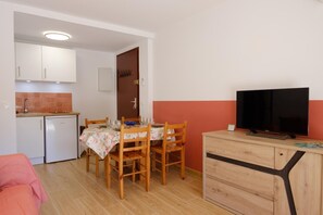 Ein kompakter Wohnbereich mit Essbereich, Küchenzeile und einem Fernseher auf einem Holzschrank.