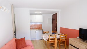 Ein kompakter Wohnbereich mit Küchenzeile, einem Esstisch für vier Personen, einer Couch und einem Fernseher.