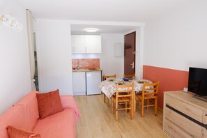 Ein kompakter Wohnbereich mit Küchenzeile, einem Esstisch für vier Personen, einer Couch und einem Fernseher.