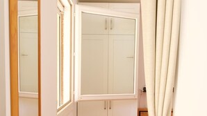 Ein Zimmer mit Holzboden, einem weißen Kleiderschrank, einem Spiegel und einem Vorhang.