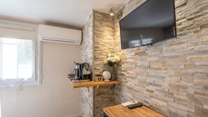 A modern kitchen with a stone backsplash, a mounted flat-screen TV, a coffee maker, and a vase with flowers. - Studio near Old Port, Panier and Station (Marseille)