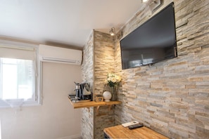 Eine moderne Küche mit Steinrückwand, einem wandmontierten Flachbildfernseher, einer Kaffeemaschine und einer Vase mit Blumen.