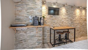 A compact room with a stone wall, a flat-screen TV, a coffee machine, a scale, and a small table with stools. - Studio near Old Port, Panier and Station (Marseille)