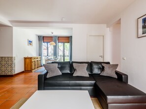 A modern living room with a black leather sofa, a dining table, and a kitchen area in the background. - Aldeia das Açoteias Apartment by Interhome (Albufeira)