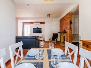 A dining area with a table set for two, a black sofa, a TV mounted on the wall, and a brick fireplace. - Aldeia das Açoteias Apartment by Interhome (Albufeira)